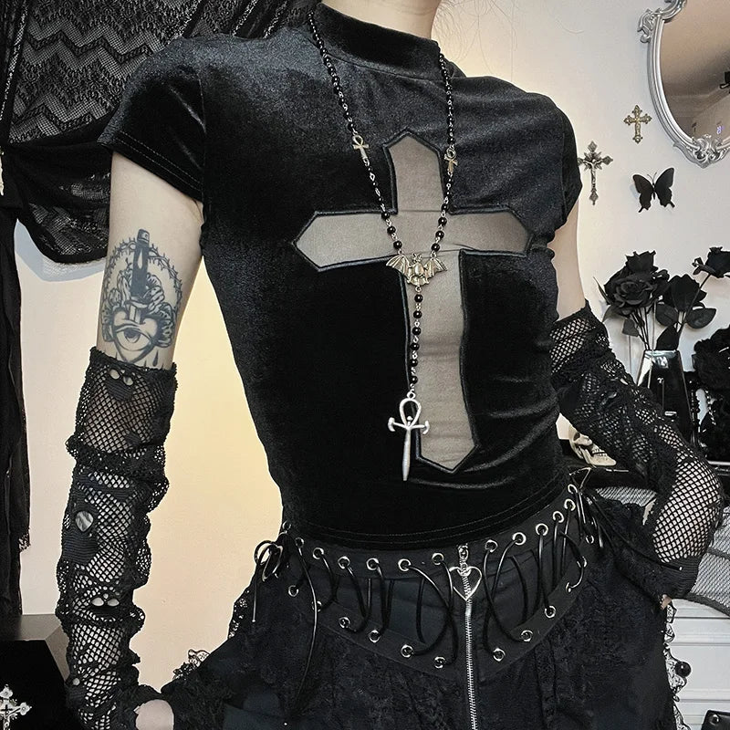 A person in a gothic style ensemble featuring the Maramalive™ Goth Dark Cross Sheer Mall Gothic Women T-shirts Grunge Aesthetic Punk Sexy Emo Black Top Streetwear Fashion Alternative Clothes paired with lace gloves and a large cross necklace. Tattoo of a crowned skull adorns the upper arm. The background is adorned with dark decor, including crosses and black flowers.