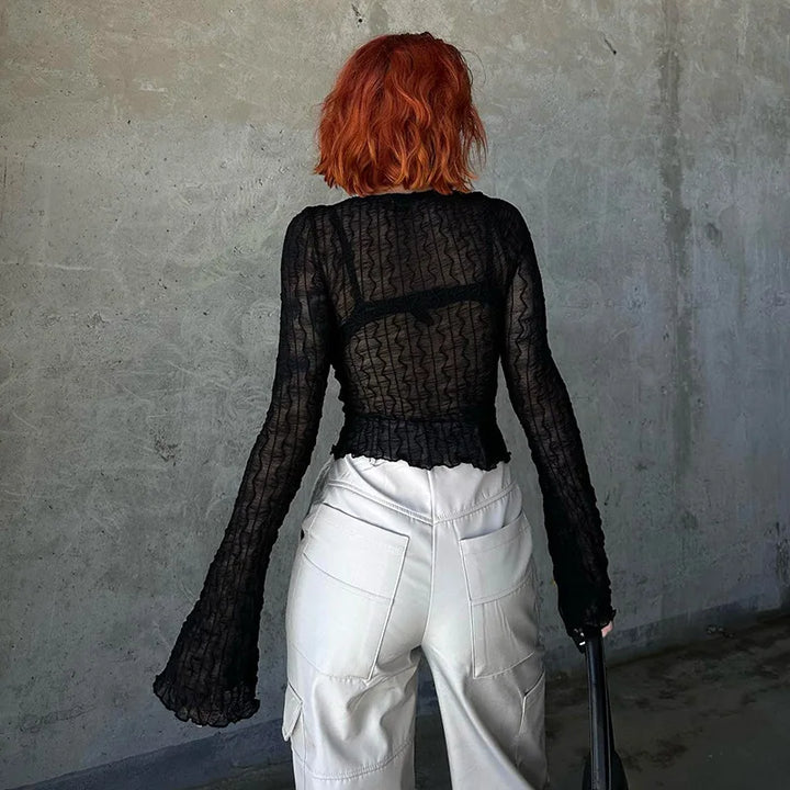 A person with red hair, wearing a black Maramalive™ Goth Dark Folds Mall Gothic Lace Up Sexy Blouses Grunge Y2k Fairycore Long Sleeve T-shirts Female Transparent Skinny Fashion Tops and white cargo pants, stands facing a gray concrete wall. The ensemble adds a touch of Gothic fashion to their appearance.