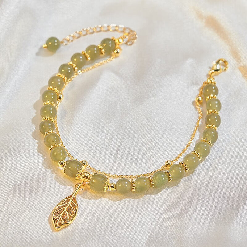 A woman wearing a Maramalive™ S925 Sterling Silver Descendants Of The Rich Hetian Jade Bracelet with a leaf and gold charm.