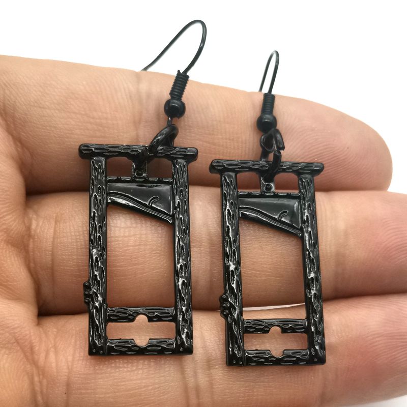 A pair of Guillotine Gothic Earrings Halloween Vintage Nature by Maramalive™ on a person's hand.