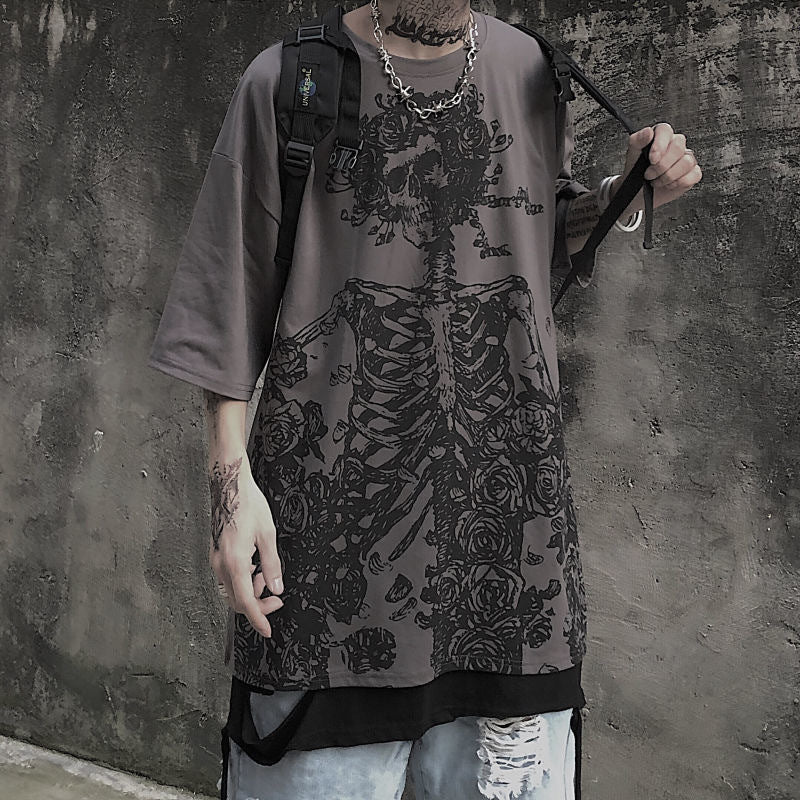 A person wearing a Maramalive™ Dark Hip Hop Tee - Perfect for Underground Rap Fans with a skeleton and floral design, holding a strap of a backpack. The background features a textured, dark wall, adding an edgy vibe to the streetwear fashion look.