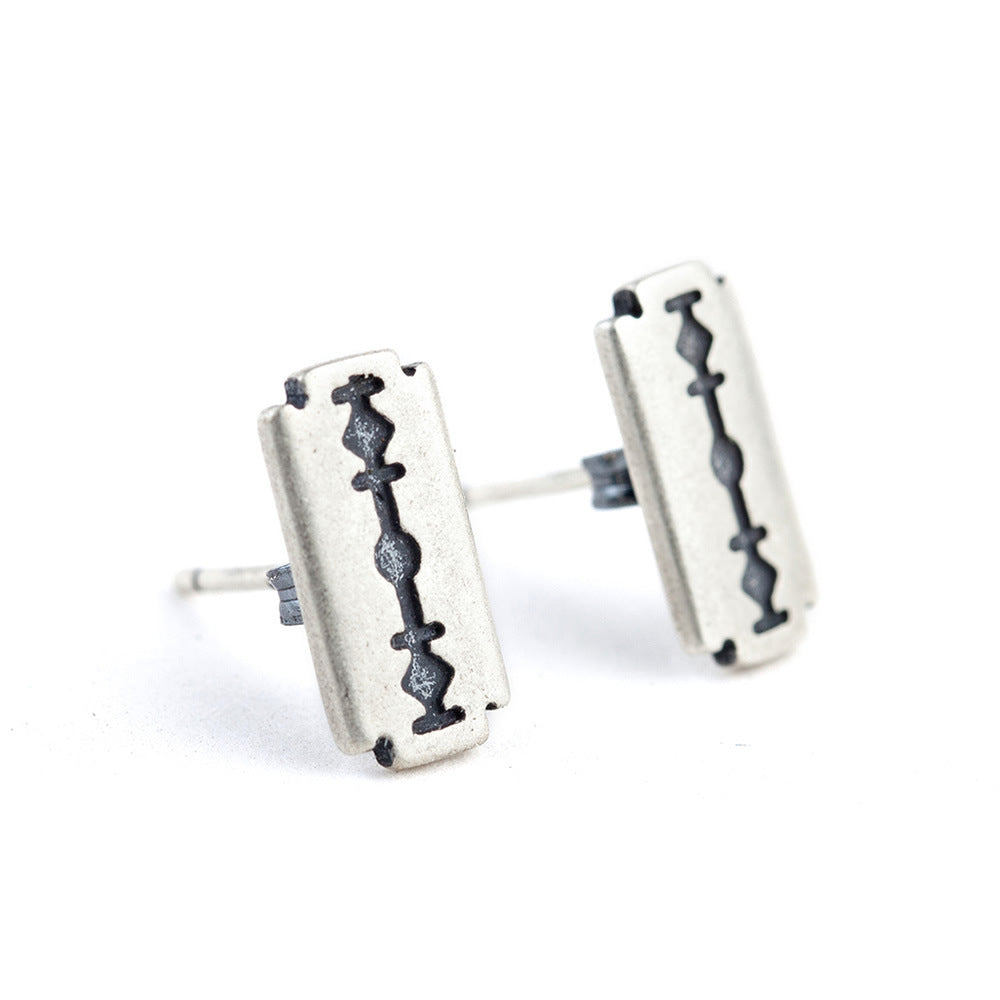 A pair of Refined Rebellion: Sterling Silver Razor Blade Gothic Ear Studs by Maramalive™ on a wooden table.
