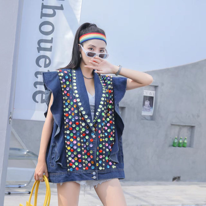 Person wearing a Maramalive™ Heavy Duty Diamond Studded Denim Vest With Wooden Ear Edge adorned with colorful buttons and beaded sequins, jeans shorts, a striped headband, and sunglasses. They are holding a yellow bag and posing near a 'Silhouette' banner and concrete wall.
