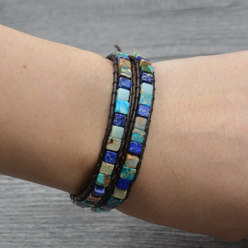 A woman's hand is holding a Multi Layer Handwoven Imperial Stone Bracelet with beads and a charm by Maramalive™.