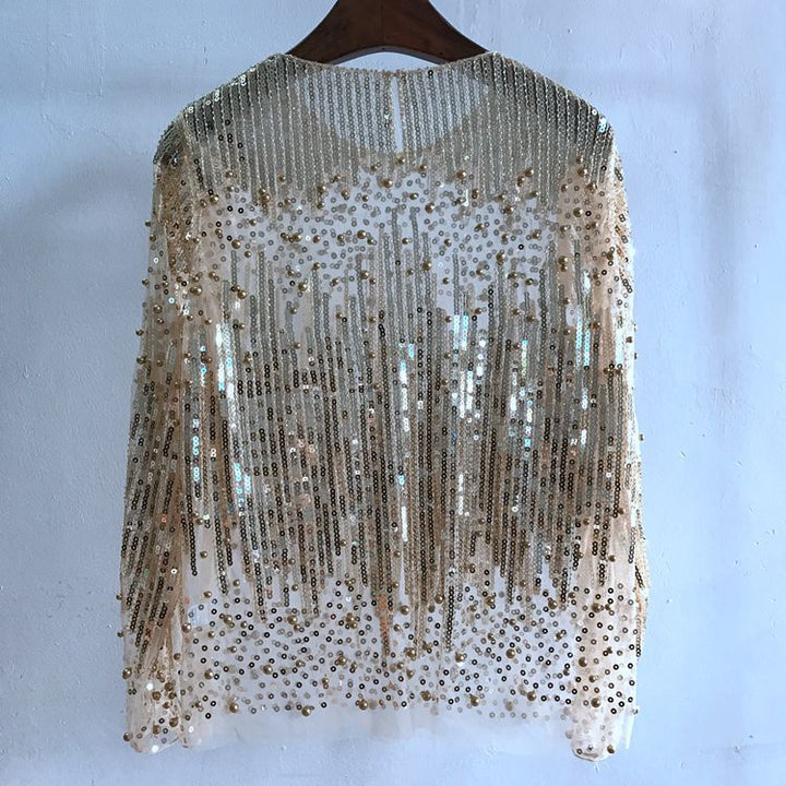 A Maramalive™ Fashion Bottoming Shirt Sequined Top For Women, embellished with gold sequins and beads, crafted from Polyester Fiber, hangs on a wooden hanger against a white wall.