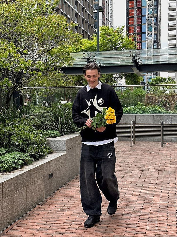 Person in a Maramalive™ Hip-Hop Street Gothic Print Knitted Sweater and pants walking on a brick pathway, holding a potted plant with yellow flowers. The scene is framed by urban greenery and tall buildings in the background, creating a striking contrast of street fashion against the geometric patterns of the cityscape.