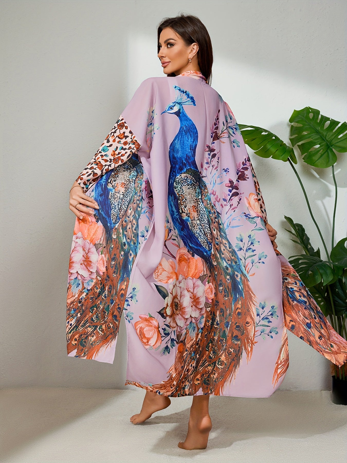 A woman is wearing a Maramalive™ Bohemian Style Women's Peacock Print Beach Cover-Up With Belt, Long Sleeves Loose Fit Vacation Kimono. She is standing barefoot on a light-colored floor next to a green leafy plant.