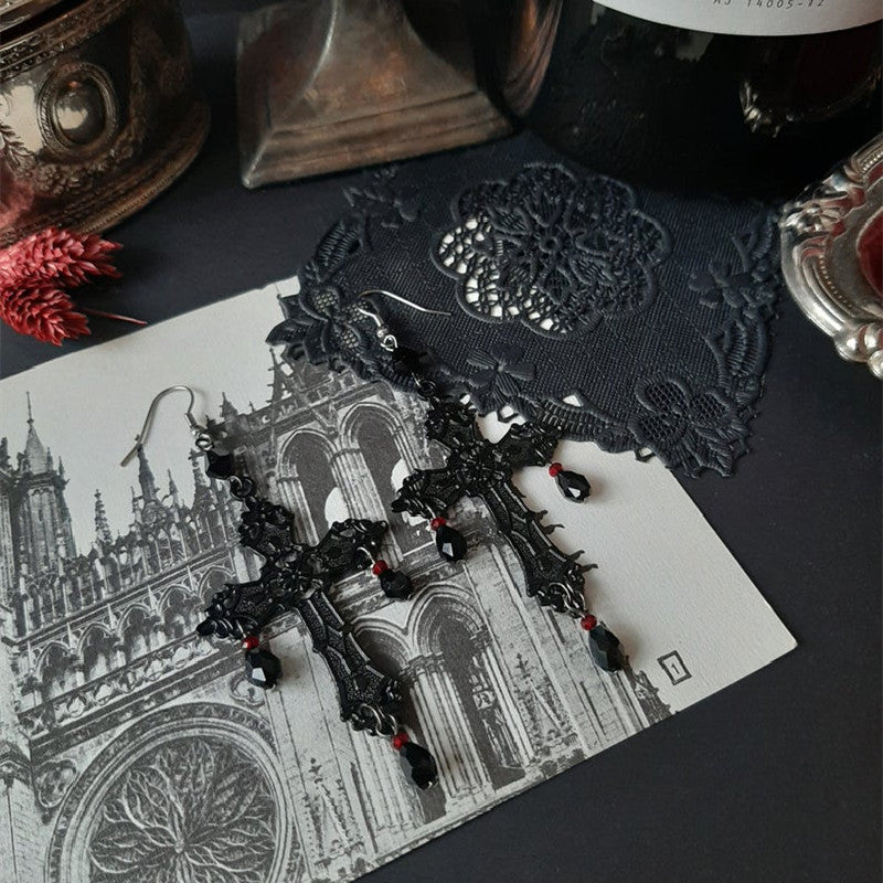 A pair of Gothic Anhe earrings by Maramalive™ on a table next to a bottle of wine.