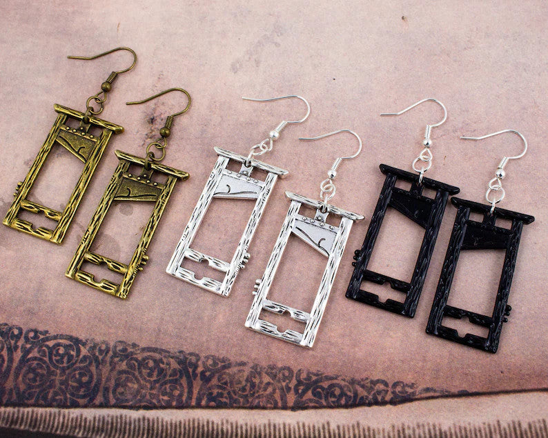 A pair of Guillotine Gothic Earrings Halloween Vintage Nature by Maramalive™ on a person's hand.