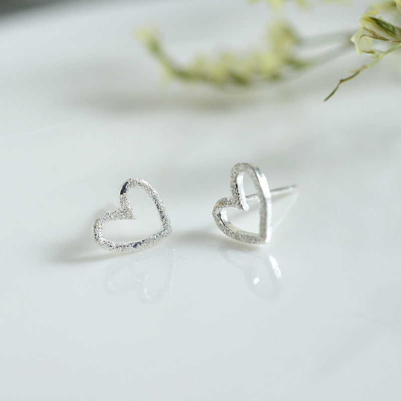 A pair of Maramalive™ S925 Sterling Silver Earrings Hollow Frosted Heart-shaped Ear Studs on top of a book.