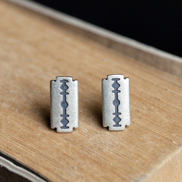 A pair of Refined Rebellion: Sterling Silver Razor Blade Gothic Ear Studs by Maramalive™ on a wooden table.