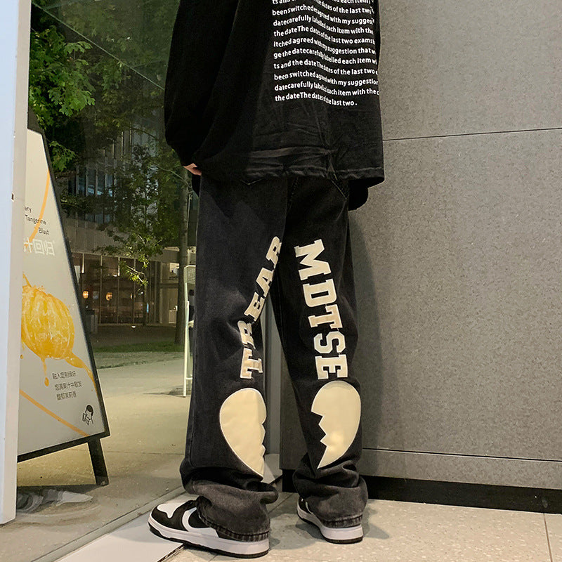 A man wearing Maramalive™ Hip-Hop Trousers with Ripped Black Denim & Lettering Embroidery 