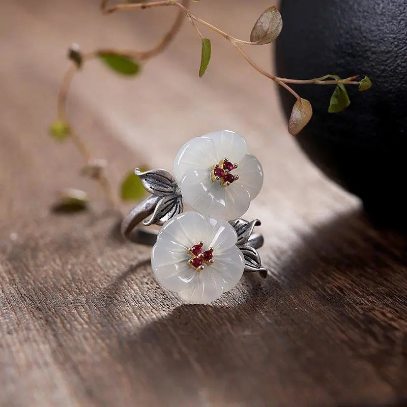 A Fashion Antique Flower Women's Ring by Maramalive™ with two white jade flowers on top of a wooden table.