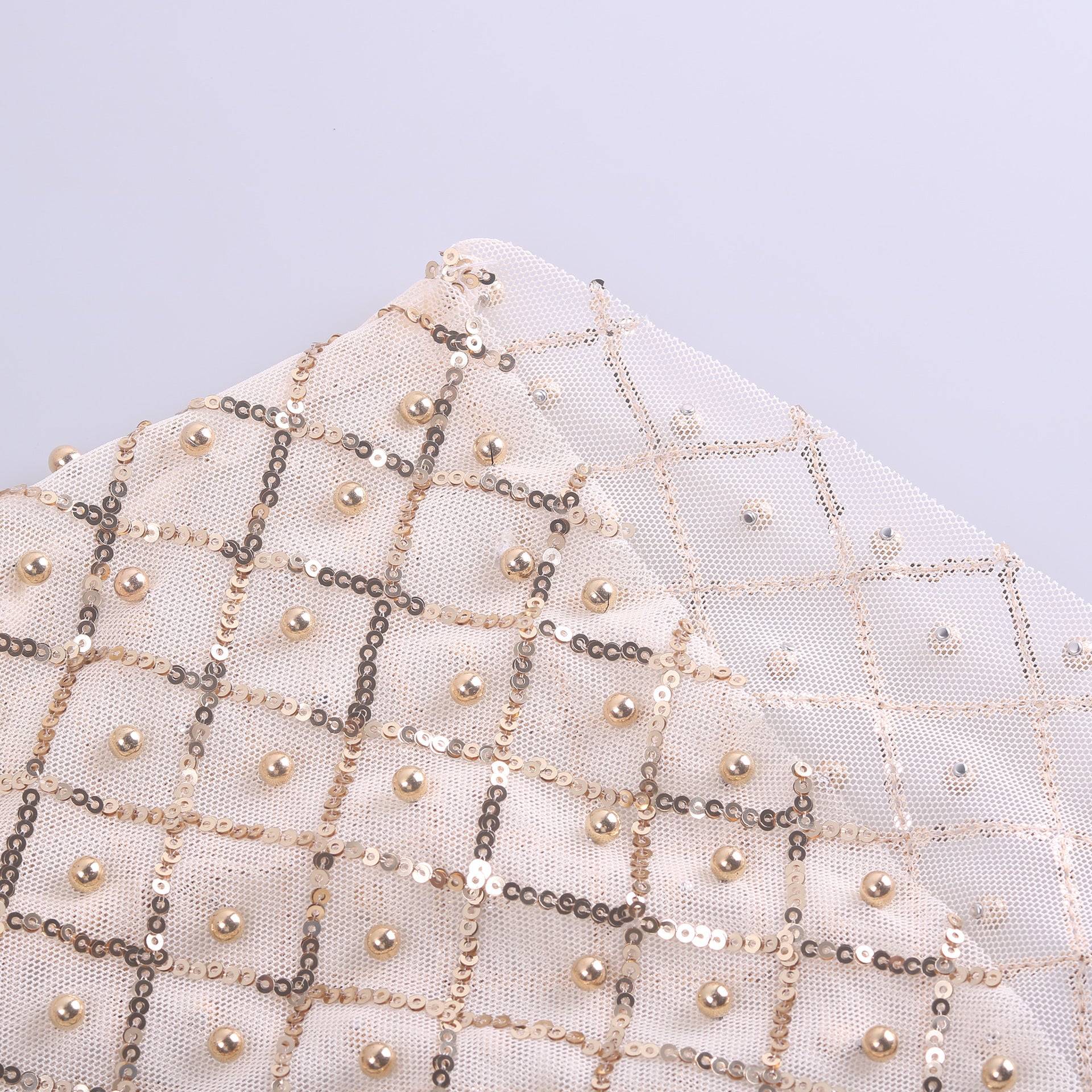 Close-up of a piece of fabric featuring a white and gold checkered pattern adorned with pearls and sequins, reminiscent of celebrity style. Crafted from durable polyester fiber, this material exudes elegance perfect for long sleeve designs. This stunning detail is part of the Mesh Studded Sequin Long-sleeved Shirt by Maramalive™.