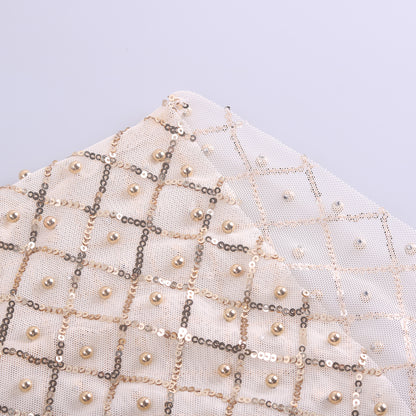 Close-up of a piece of fabric featuring a white and gold checkered pattern adorned with pearls and sequins, reminiscent of celebrity style. Crafted from durable polyester fiber, this material exudes elegance perfect for long sleeve designs. This stunning detail is part of the Mesh Studded Sequin Long-sleeved Shirt by Maramalive™.
