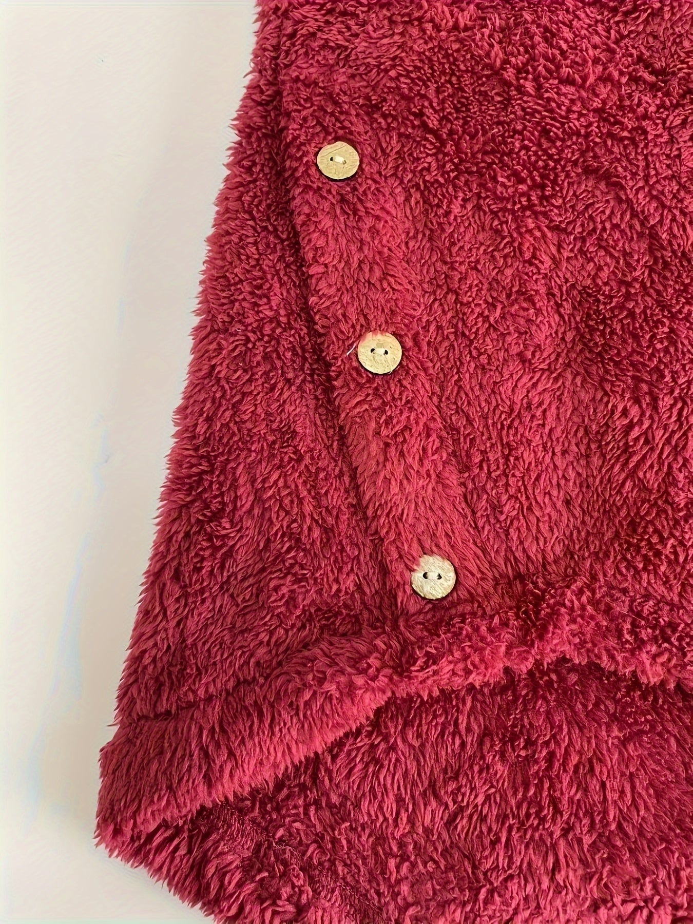 A close-up photo of a red, fuzzy fabric with three white buttons stitched along one edge, reminiscent of the Maramalive™ Plus Size Casual Sweatshirt, Women's Plus Slogan & Cat Print Fleece Button Decor Long Sleeve Cat Ear Button Decor Sweatshirt With Pockets.
