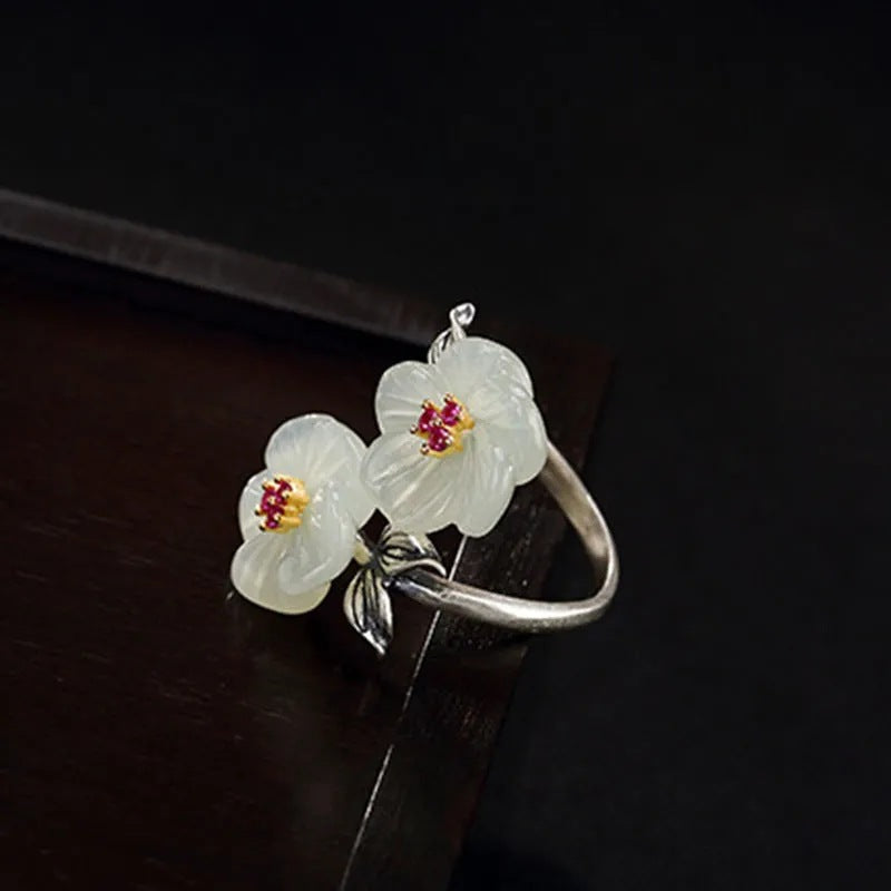 A Fashion Antique Flower Women's Ring by Maramalive™ with two white jade flowers on top of a wooden table.