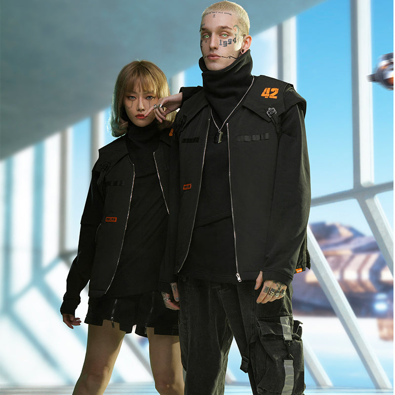 Two individuals dressed in futuristic black and green military-style clothing, showcasing youth fashion, stand indoors beside a large window with a view of a spaceship. One person wears a Maramalive™ Punk Fake Two-piece Plush And Thick High Neck Loose Top made from 100% cotton, while the other has tattoos and short hair.