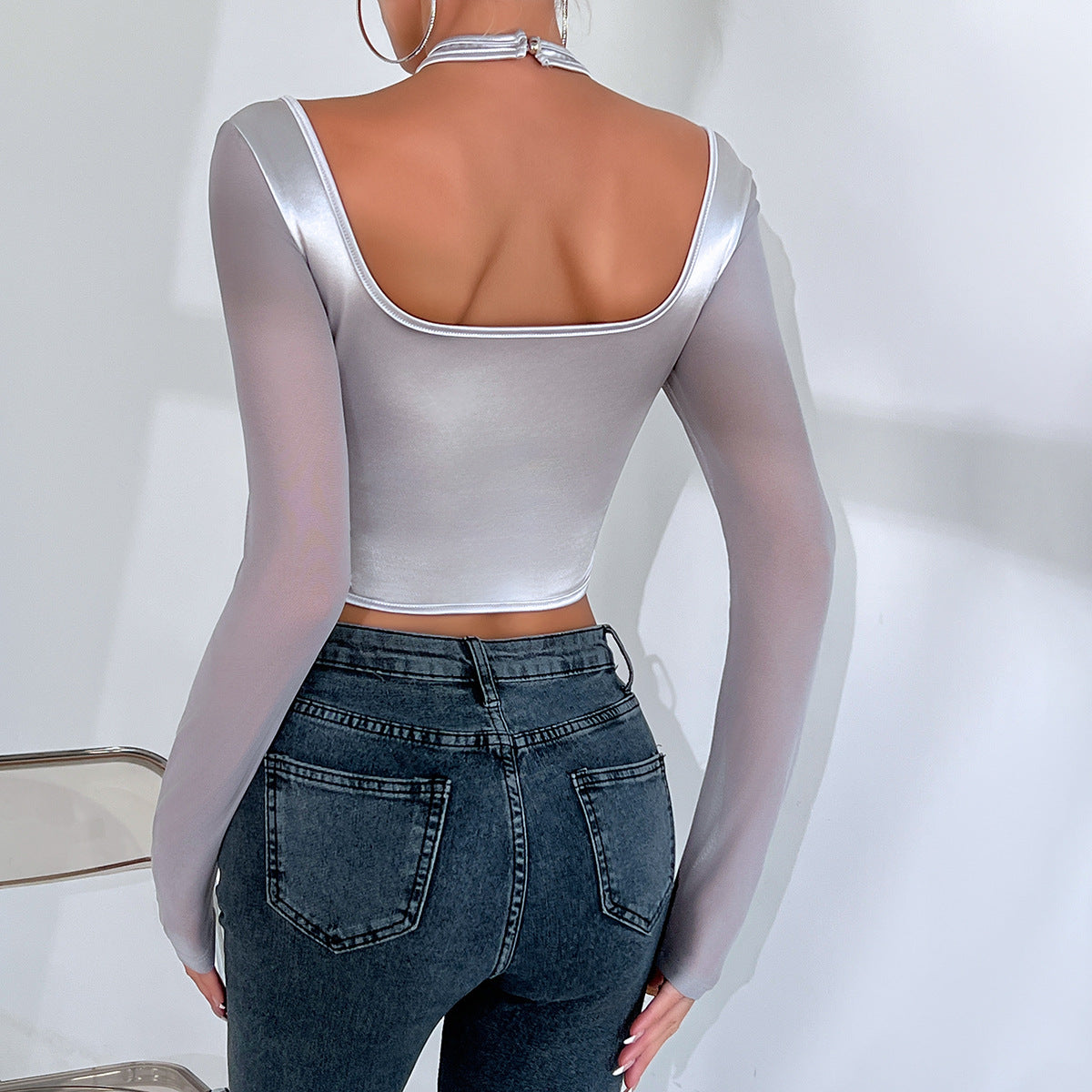A person wearing a Maramalive™ Hot Girl Low-cut Sexy See-through Mesh Patchwork Halter Top Female and jeans stands facing away from the camera, capturing an essence of street fashion.