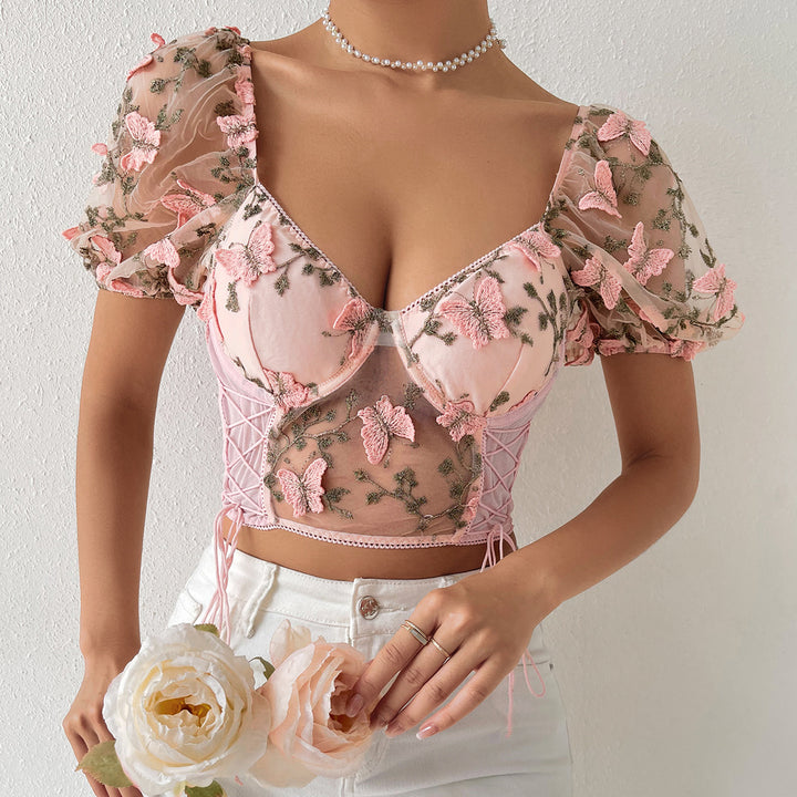 Person wearing a pink, floral-embroidered Ladies New Hot Girl Backless See-through Camisole by Maramalive™ with puffed sleeves and lace-up detailing, reminiscent of European and American style, holding a bouquet of white flowers.