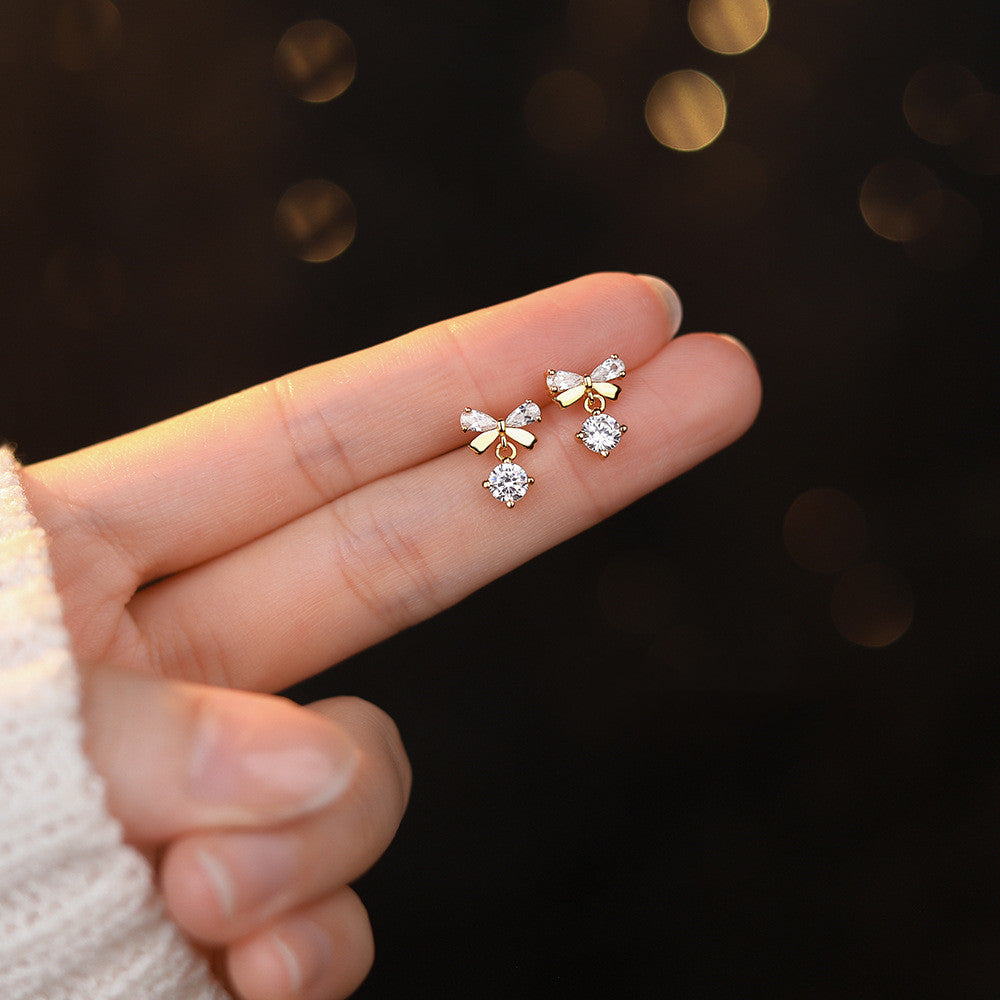 A woman wearing a white shirt and a pair of Maramalive™ Women's Graceful And Fashionable Pure Silver Zircon Bow Stud Earrings.