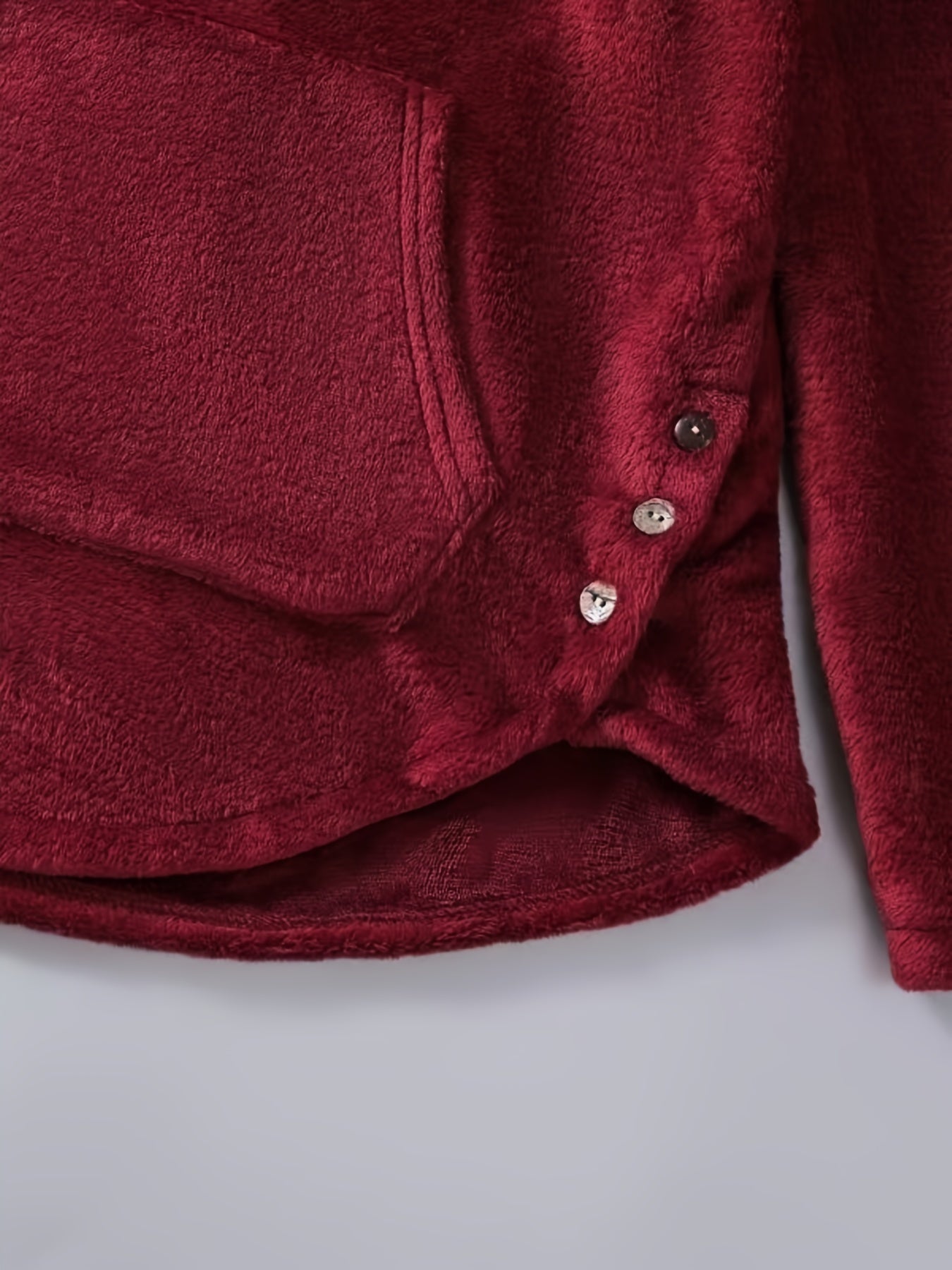 Close-up of a maroon, plush fabric top with a pocket and four buttons on the side, resembling cozy comfortable winter wear. The texture appears soft and fuzzy. This is the Graphic Print Fluffy Loose Cat Ears Hoodie, Casual Hooded Pocket Fashion Long Sleeve Sweatshirt from Maramalive™.
