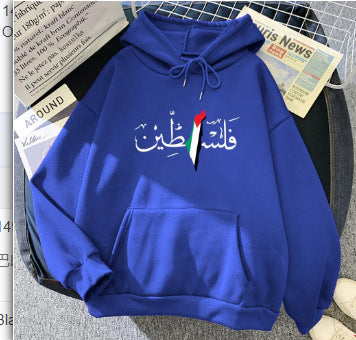 A Maramalive™ Autumn And Winter Fleece Warm Hoodie Jacket Casual Sweatshirt with white Arabic text and a heart-shaped design, incorporating the colors of the Palestinian flag (black, white, red, and green), lies on a gray surface next to newspapers. Made of polyester, this men's hoodie combines style with cultural pride.