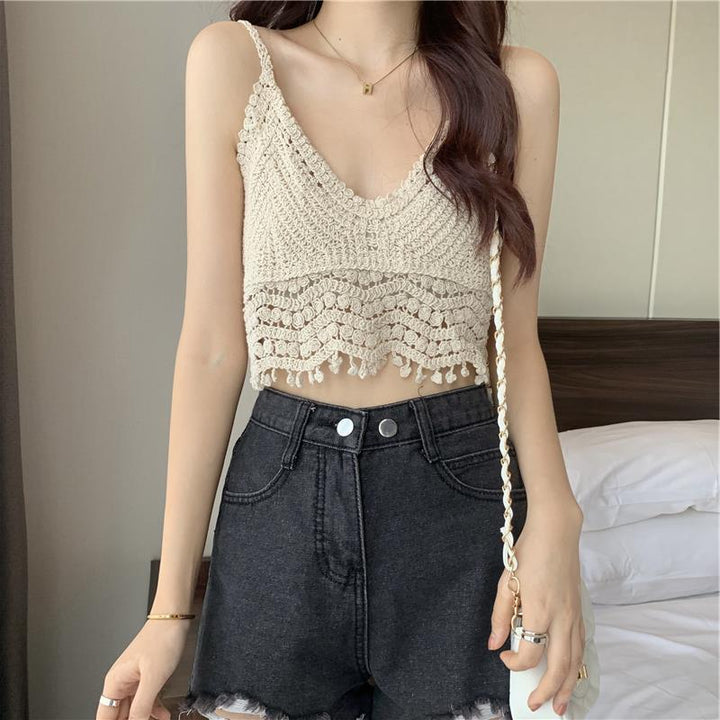 A woman is wearing the Crocheted Two-piece Set Female Summer New Western Style Blouse Top by Maramalive™ and high-waisted black shorts. She has a white purse slung over her shoulder and is standing in front of a bed with white bedding, exuding a fresh and sweet style.