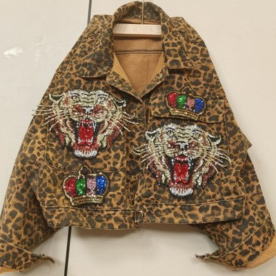 A Leopard Print Studded With Nails Bead Mesh Gauze Stitching Denim Short Coat Female, crafted from triacetate fiber, features two embroidered tigers with open mouths and crowns on the front. The coat is displayed hanging on a hanger against a plain background and is available in various size options. This distinctive piece is part of the Maramalive™ collection.